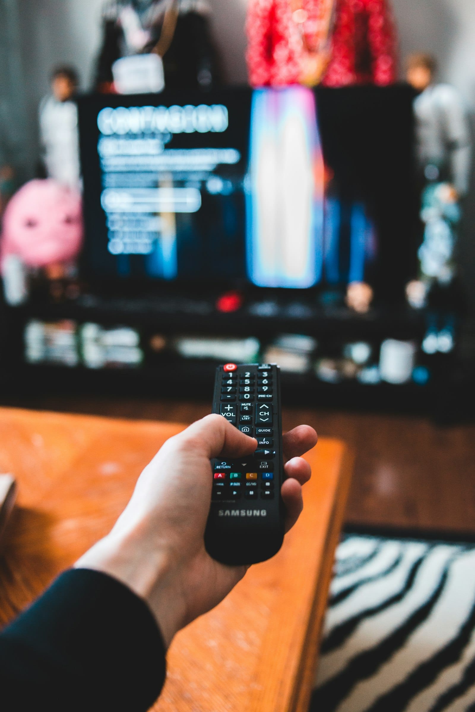 Hand pointing a TV remote at a television in a living room