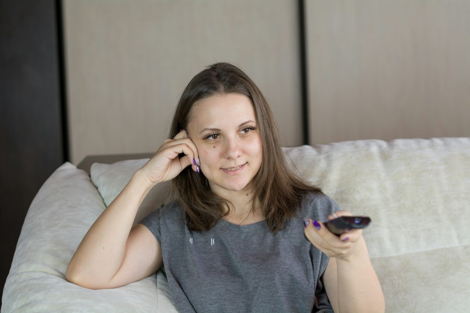 Woman relaxing on a sofa, pointing a remote at the TV
