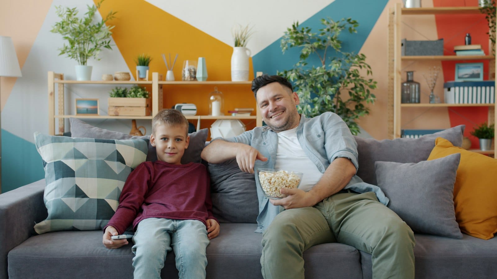 Father and son relaxing on a sofa with popcorn, watching TV at home